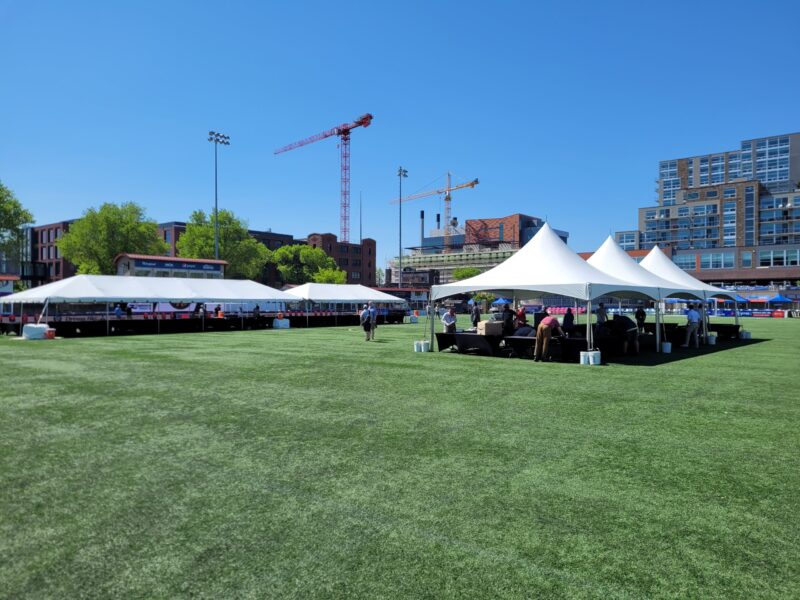 a large grassy field with white tents and buildings in the background